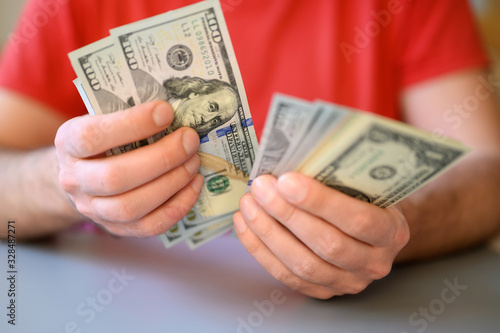 men's hands hold and count 100, 50 and 1 dollar bills on gray table