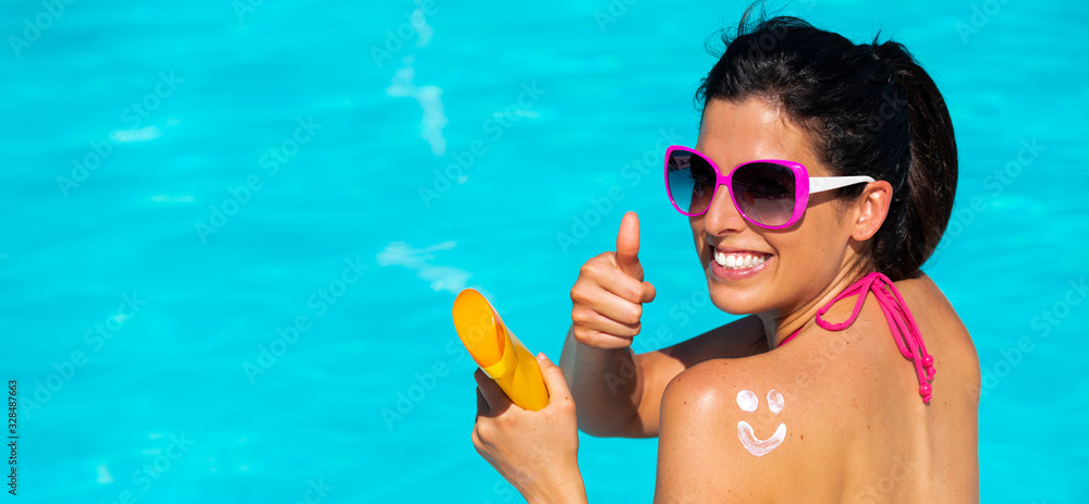 Banner of young tanned woman applying sunscreen on her back at swimming pool. Summer tanning and relaxing vacation concept. Skin care and uv protection. Happy smiley face drawn with suntan lotion.