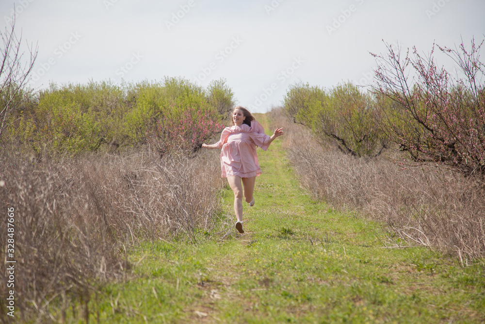 Beautiful blonde woman in pink dress walks through the flowering garden Beautiful blonde woman in pink dress walks through the flowering garden