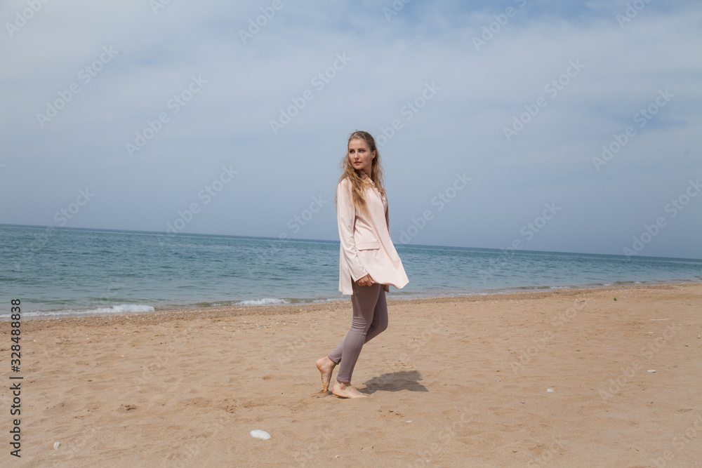 Beautiful blonde woman walks on an empty beach by the ocean