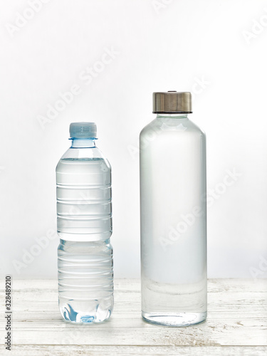 Reusable glass water bottle versus plastic water bottle on white table