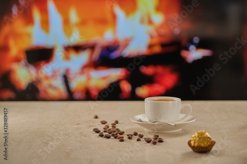 Cup of coffee on a marble table against the background of the fireplace. Coffee beans, chocolate candy on the table.