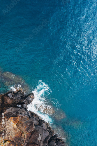 Top aerial view of turquoise Atlantic ocean water waves crashing on rocks on the Portuguese Madera island seashore.