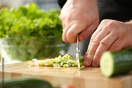Cook holds knife in hand and cuts on cutting board green onions for salad or fresh vegetable soup with vitamins. Raw food and vegetarian recipe book in modern society popular concept.