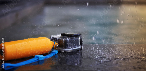 Action camera in waterproof case and floater grip on poolside with water rain drops in stop action and motion blur