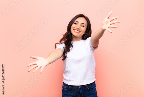 young latin pretty woman smiling cheerfully giving a warm, friendly, loving welcome hug, feeling happy and adorable against flat wall photo