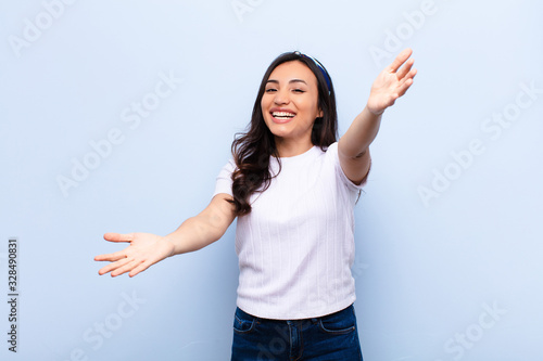 young latin pretty woman smiling cheerfully giving a warm, friendly, loving welcome hug, feeling happy and adorable against flat wall photo