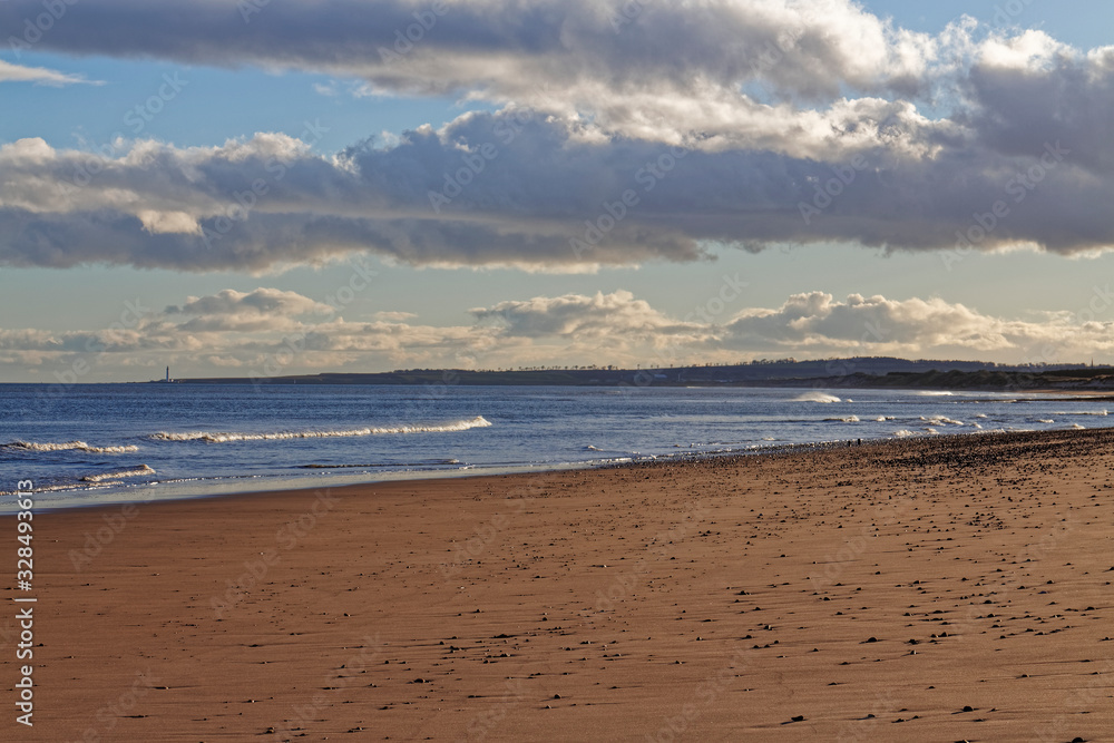 St Cyrus beach with the tide out, looking towards Montrose and Scurdie Ness Lighthouse on a golden February evening.