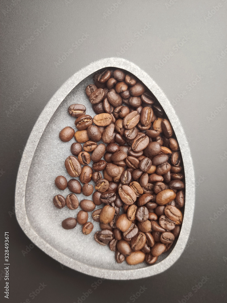 Roasted coffee beans in a ceramic bowl on a black background.