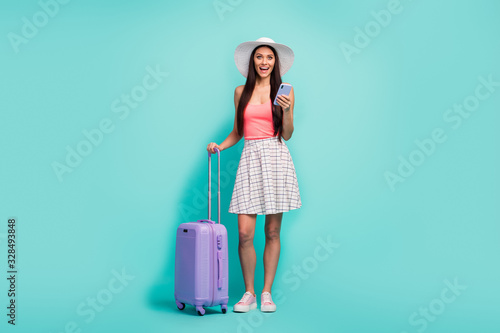 Full size surprised girl travel use smartphone impressed fast hotel reservation scream wow hold bag wear sunhat white checkered plaid skirt pink tank-top isolated turquoise color background