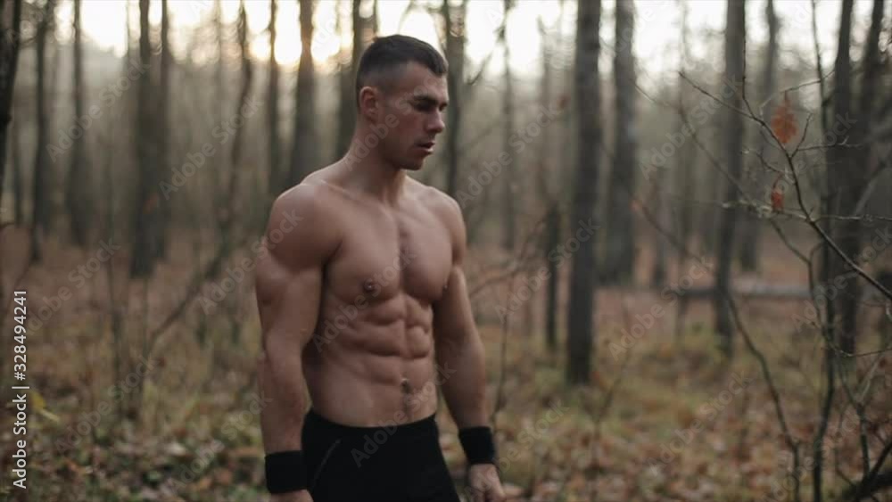 Muscular Male Athletic With Naked Torso Stands In The autumn forest. leaves fall from trees. Slow motion. Muscular Male Athletic With Naked Torso Stands In The autumn forest. leaves fall from trees. Slow motion.