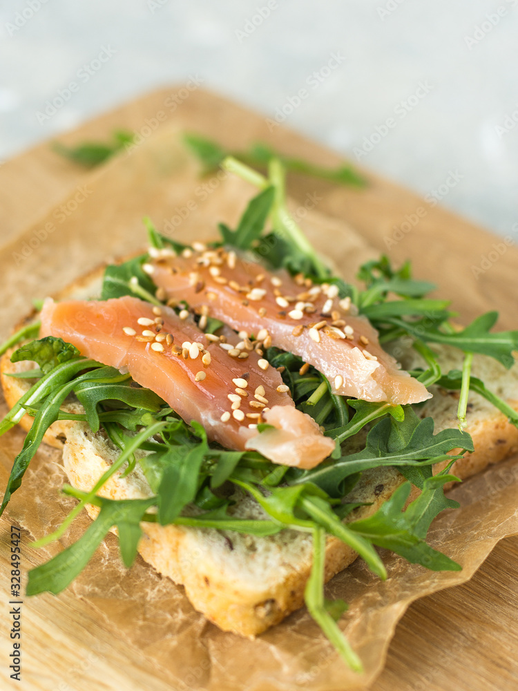 Cereal toast with arugula and trout on paper and wooden board close-up Cereal toast with arugula and trout on paper and wooden board close-up