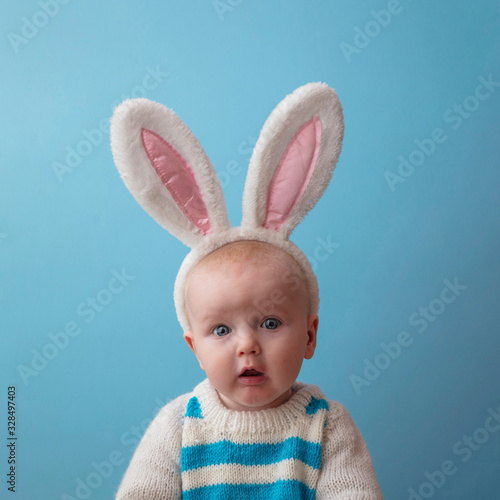 Sticker Sad looking baby wearing white easter bunny ears against a blue background