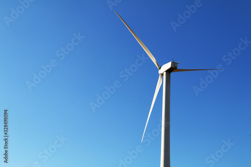 single shining white wind turbine bright blue sky © DrewTraveler