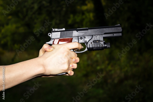 Female hands holding a gun on a dark background. A dangerous situation with a gun