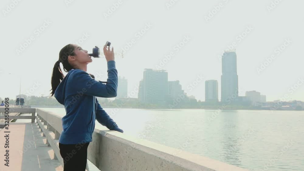 Attractive sporty girl happily drinking water after workout beside the sea and the city background. Attractive sporty girl happily drinking water after workout beside the sea and the city background.