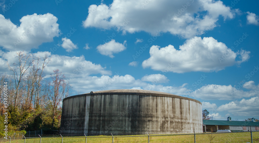 A huge, round, concrete water tank in a green field under blue skies beyond a white fence