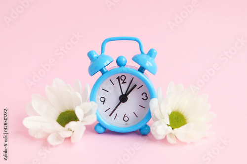 Concept of early spring, blue alarm clock with flowers on a pink background