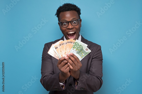 Cheerful young african businessman holding money over blue background photo