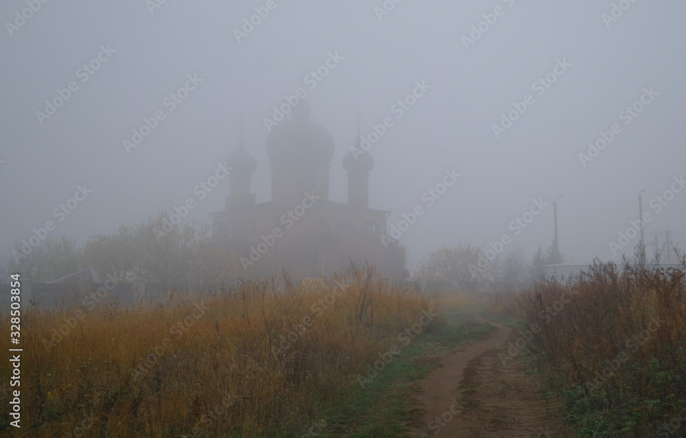 Autumn landscape with fog and the road to the church