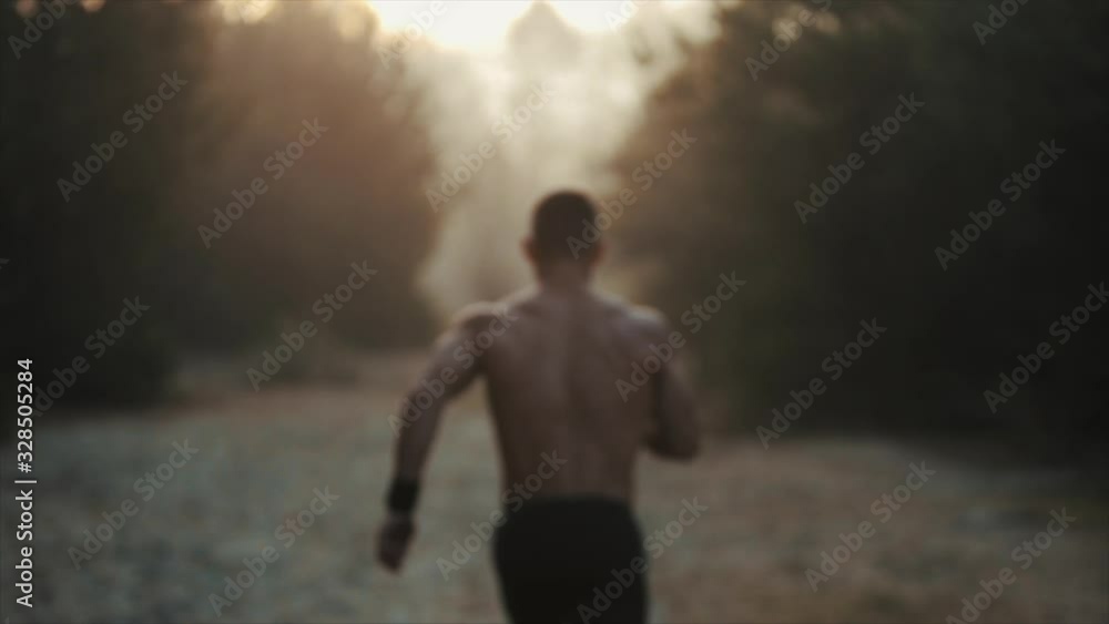 Running sport man. Fit muscular young male runner with naked torso sprinting beetwen trees against dawn, sunrise. Slow motion Running sport man. Fit muscular young male runner with naked torso sprinting beetwen trees against dawn, sunrise. Slow motion
