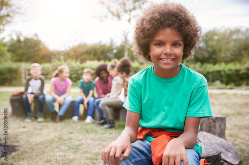 Portrait Of Boy On Outdoor Activity Camping Trip Sitting Around Camp Fire With Friends