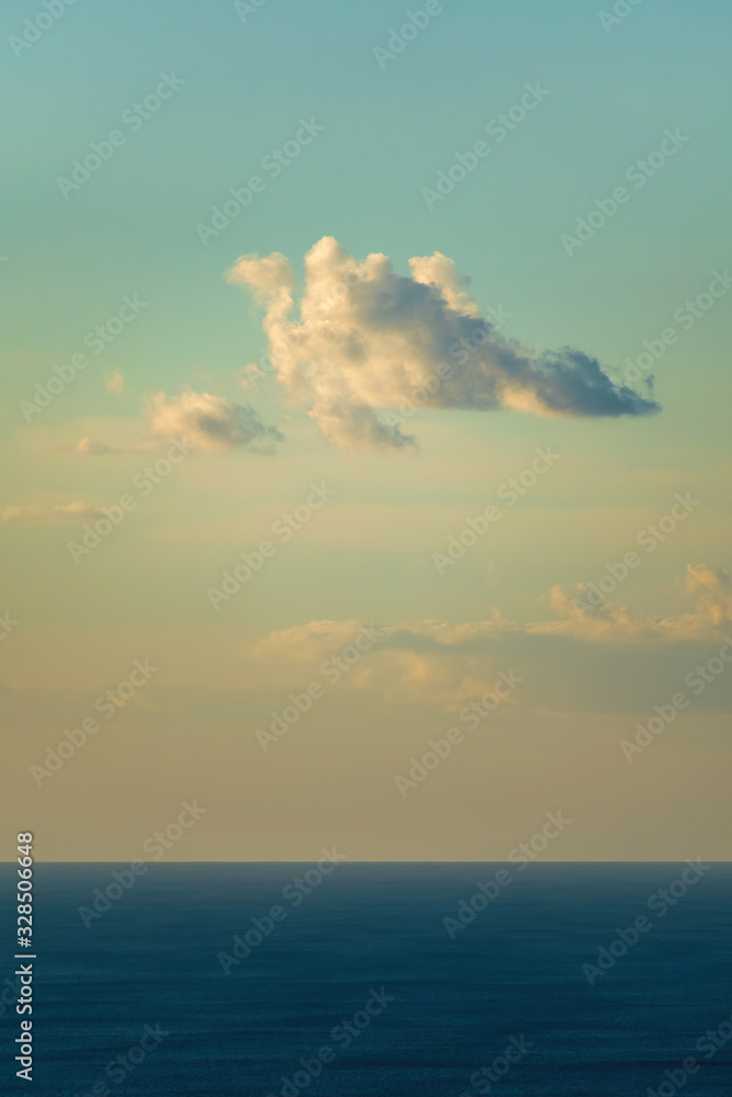 Vertical view of cloud flying over deep blue ocean surface in yellow evening light