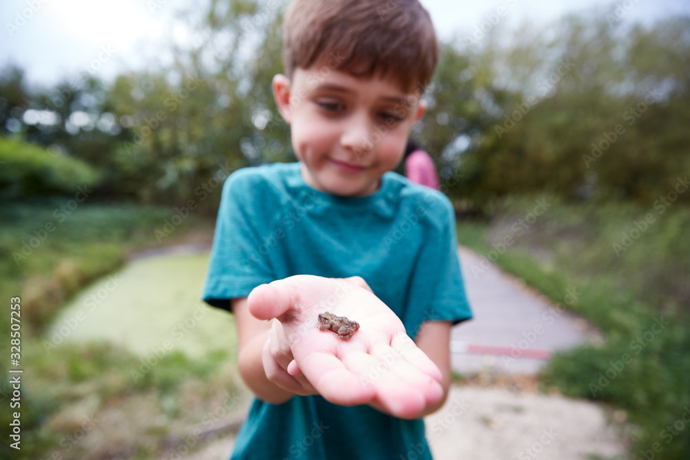Boy Holding Small Frog As Group Of Children On Outdoor Activity Camp Catch And Study Pond Life Boy Holding Small Frog As Group Of Children On Outdoor Activity Camp Catch And Study Pond Life