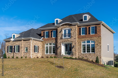 Newly constructed American luxury house symmetric facade covered  by stone and brick, arched decorative white casement windows sash separated by grills, accent trim, dormer on roof, side vinyl