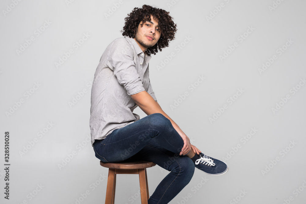 Young man sitting on a small stool against white wall background Young man sitting on a small stool against white wall background