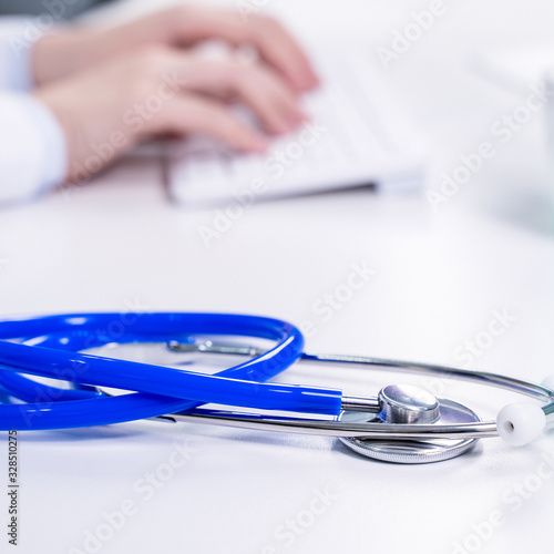 Business concept - Young female doctor woman working at office with computer  typing electronic medical record  white table background  close up  copy space