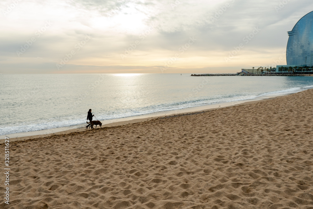 Man walking dog on the beach at sunrise. Barcelona, Spain.