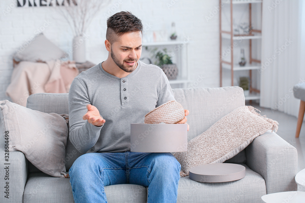 Displeased young man unpacking parcel at home