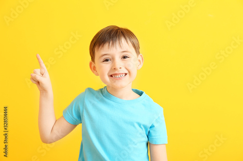 Happy smiling little boy pointing at something on color background