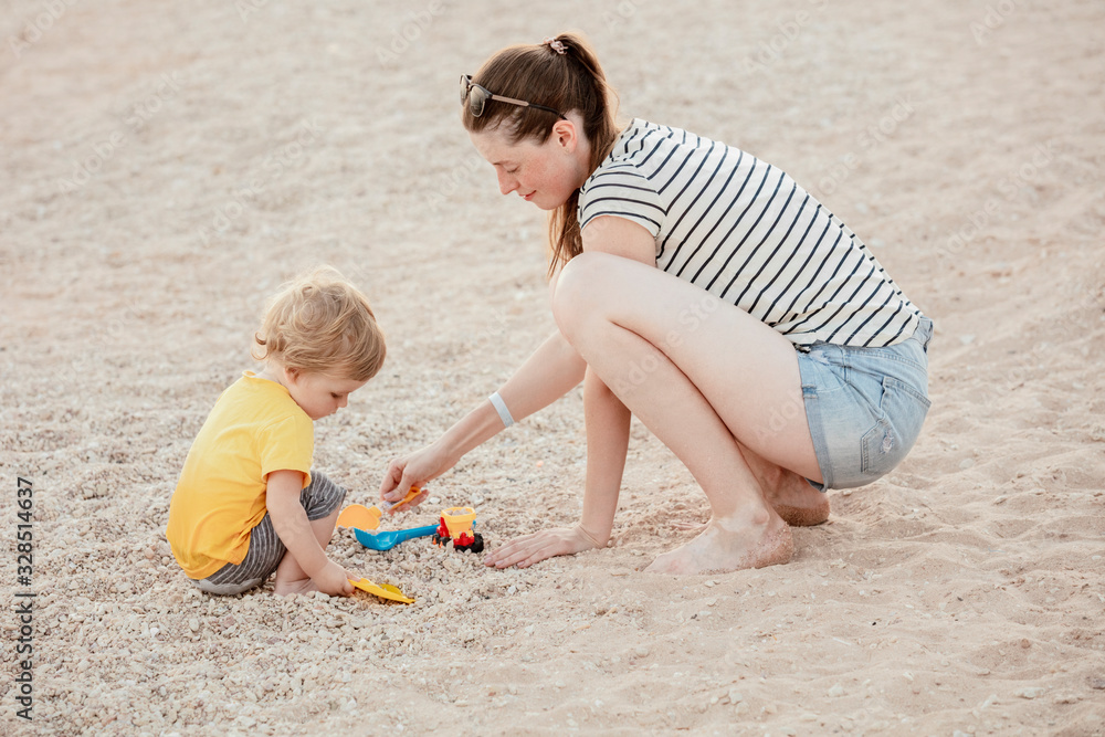Happy mother and son play on the beach. Mom and baby play in the sand. Mom play with a toddler on the seaside. Mother's love. Lifestyle. Sunny day. Summer rest. Family vacation. Mother's day. Happy mother and son play on the beach. Mom and baby play in the sand. Mom play with a toddler on the seaside. Mother's love. Lifestyle. Sunny day. Summer rest. Family vacation. Mother's day.