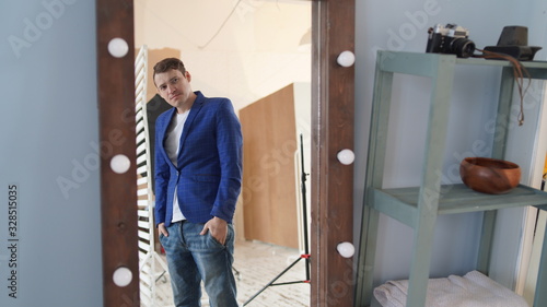 A handsome man looks in the mirror. A side view of a young man in a mirror in a modern bedroom