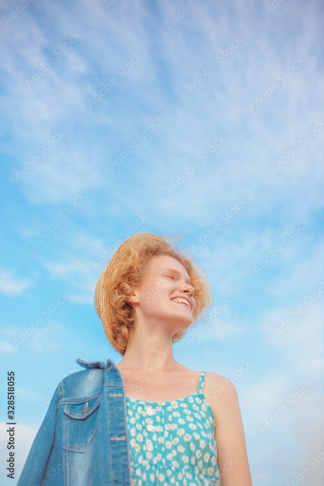 young curly redhead woman in straw hat, blue sundress and jeans jacket standing on blue sky background. Fun, summer, fashion, shooting, travel, youth concept. Copy spase young curly redhead woman in straw hat, blue sundress and jeans jacket standing on blue sky background. Fun, summer, fashion, shooting, travel, youth concept. Copy spase