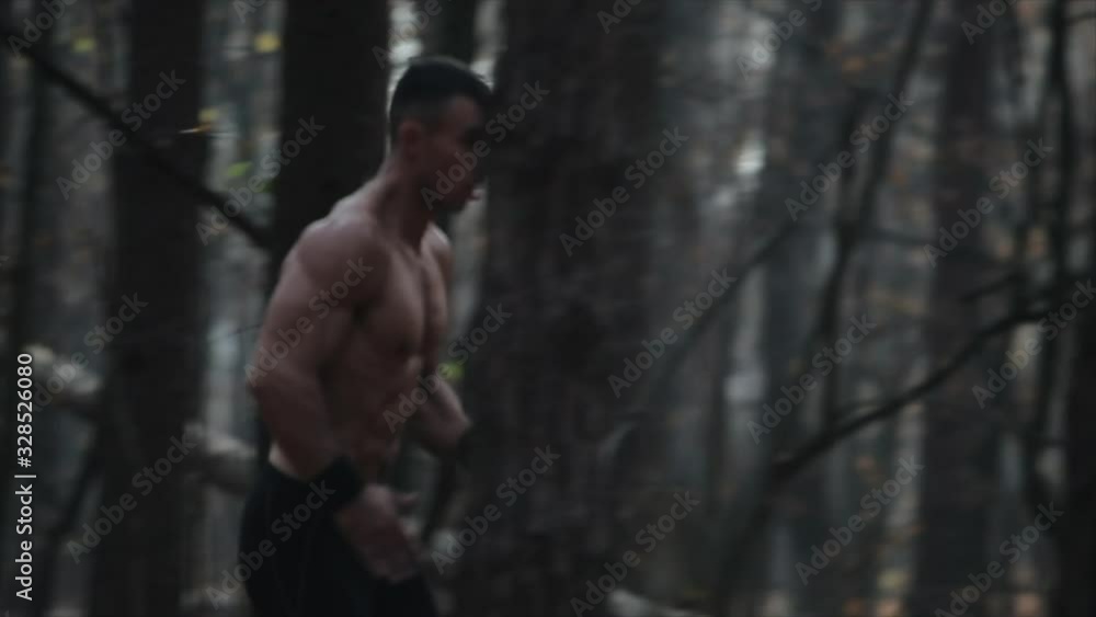 young muscular runner runs in the forest. Running between the trees. Slow motion