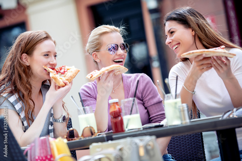 Happy female friends eating pizza in cafe.