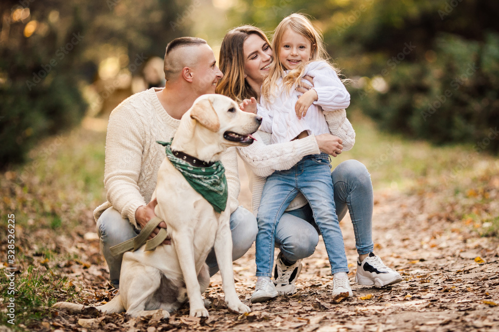 Obraz premium Happy beautiful family with dog labrador is having fun together walking the in park.