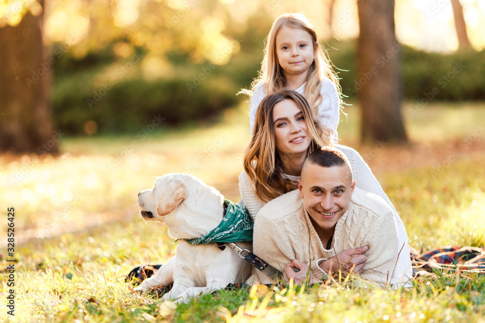 Fototapeta premium Happy family is having fun with dog labrador are lying on green grass in park.