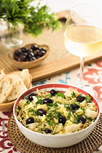 Table set for a dinner. A codfish salad with potatoes stick, black olives and parsley is being served on a bowl, an typical portuguese dish. photo