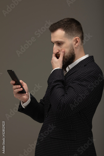 Closeup of a serious and worried businessman using cellphone against grey background.