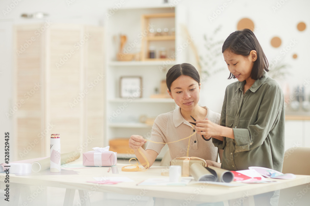 Horizontal portrait of teenage girl cutting ribbon for gift box decoration, young woman helping her, copy space Horizontal portrait of teenage girl cutting ribbon for gift box decoration, young woman helping her, copy space