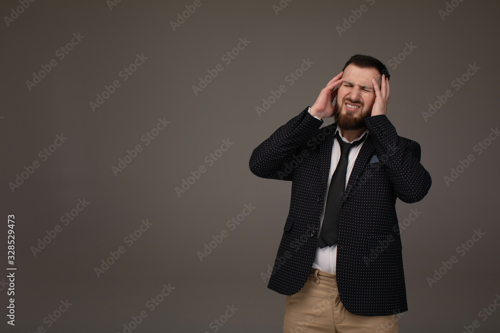 Young handsome bearded business man wearing suit over grey background with hand on headache because stress. Suffering migraine.