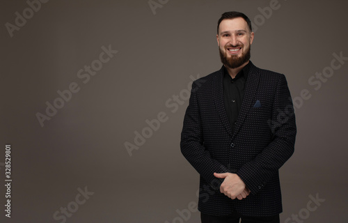 Handsome young bearded man on grey background looking at camera. Portrait of laughing young man.