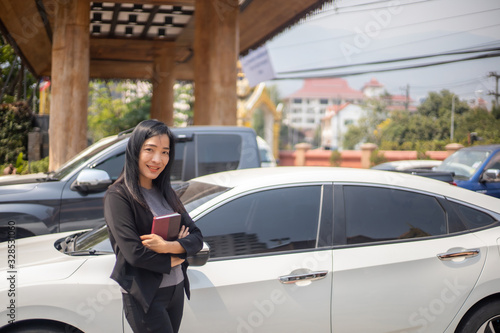 The beautiful Asian woman wearing black suit is posing next to the white car in the sunny day during her working day.  © guidenuk