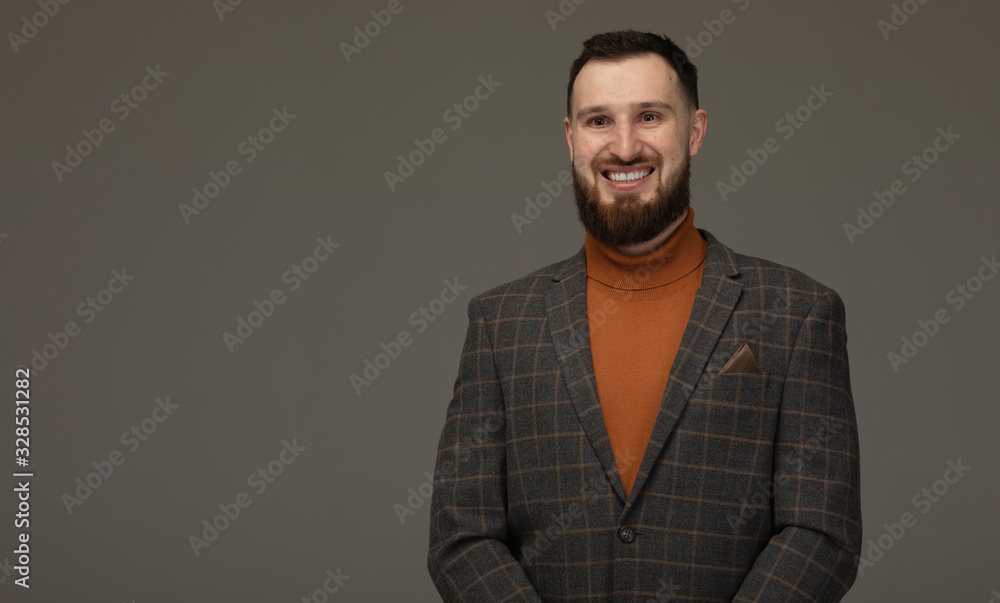 Handsome young bearded man on grey background looking at camera. Portrait of laughing young man. Handsome young bearded man on grey background looking at camera. Portrait of laughing young man.