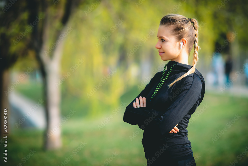 Beautiful young woman trainer standing on the park running with cross hands and looking at the camera inviting to sport and listening to music with wireless headphones - motivation health photo Beautiful young woman trainer standing on the park running with cross hands and looking at the camera inviting to sport and listening to music with wireless headphones - motivation health photo