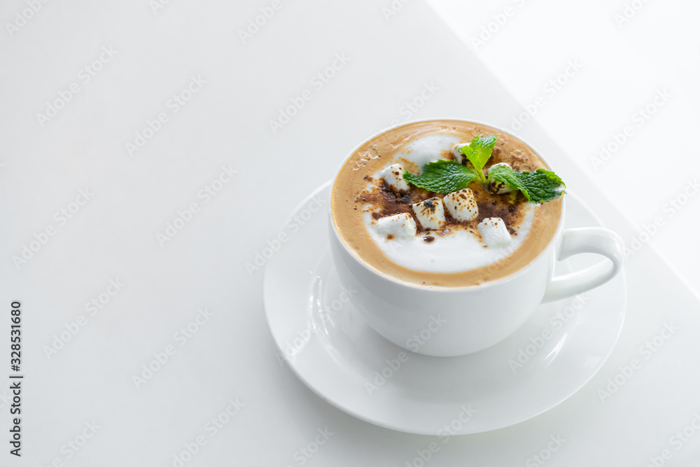 Close-up of Butterscotch latte coffee with marshmallow in a white cup and saucer on white table background. Close-up of Butterscotch latte coffee with marshmallow in a white cup and saucer on white table background.